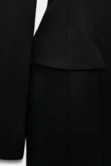 Vestido corto negro de cuello redondo y manga larga, con detalle de falsos bolsillos con solapa en el delantero y cierre de cremallera oculta en la espalda.