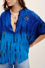 Camisa de viscosa con estampado tie-dye en tonos de azul y negro, de manga corta, cierre frontal con botones y bordados decorativos en el frente.