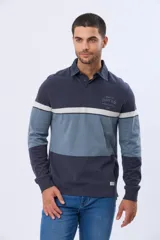 Remera polo de manga larga con diseño de bloques de color en tonos azul y gris. Presenta cuello clásico con cierre de botones, puños elásticos y una estampa bordada en el pecho.