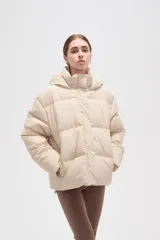 Campera puffer color beige con diseño capitoneado, capucha integrada y cierre frontal oculto. Presenta bolsillos laterales y un corte holgado.