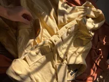 Sobre camisa de pana color amarillo, de manga larga, con botones forrados y un gran parche rectangular en la espalda con diseño de sol bordado en tonos tierra y azul claro.