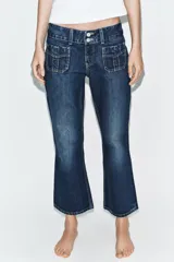 Jeans de tiro bajo y corte flare, confeccionados en denim azul con lavado localizado. Presentan bolsillos de plastrón en el delantero, trabillas para cinturón y cierre frontal con cremallera y doble botón metálico.