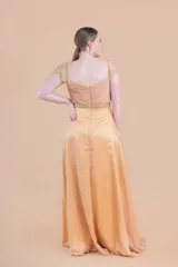 Vestido largo de fiesta color oro, confeccionado en gasa de seda natural con corsé drapeado, mangas y faja en tul bordado.