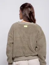 Sweater negro peludito de manga larga y cuello a la base con puños en las mangas y un bolsillo de nylon frontal con solapa y botón.