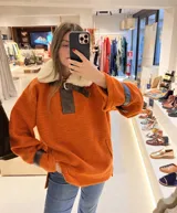 Buzo naranja con cuello de piel sintética color crema, cierre con hebilla de cuero marrón y detalles de cuero en puños y hombros.