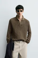 Polo de punto color marrón oscuro, de calce regular, con cuello solapa y abertura frontal en V. Presenta tejido con trencitas verticales.