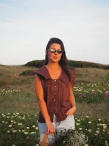 Blusa sin mangas de lino color marrón chocolate, con cuello marinero amplio y cierre frontal de botones con detalles de volados fruncidos a los lados.