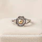Anillo de plata con diseño de flor y detalle central dorado.
