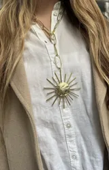 Collar de bronce con cadena de eslabones alargados y un dije central con forma de sol, compuesto por un centro redondo texturizado y rayos de diferentes longitudes.
