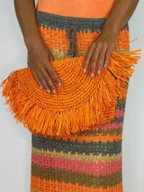 Cartera de mano tipo sobre color fucsia, confeccionada en rafia con flecos.