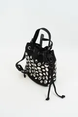 Cartera tipo bucket bag de gamuza negra, decorada con múltiples tachas metálicas plateadas de forma circular. Cuenta con cierre de cordón ajustable y asa superior.