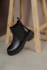 Botas tipo Chelsea de cuero con acabado vintage, diseño de caña media con paneles elásticos laterales y suela track robusta.