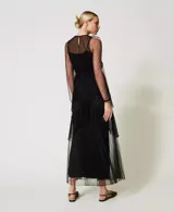 Vestido largo de tul negro con volantes plisados e inserciones de encaje. Presenta un escote redondo con lágrima, manga larga transparente, cremallera invisible lateral, cinturón fino de la misma tela y combinación, de corte ancho.