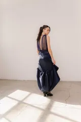 Pollera midi de tafeta color negro, con diseño asimétrico de corte mullet (más corta adelante y larga atrás), tiro alto y detalle de volado fruncido en el ruedo.