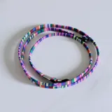 Cuerdita para lentes de tela tejida con diseño multicolor a rayas. Cuenta con terminales metálicos y sujetadores de goma negros en los extremos.