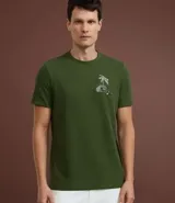 Remera verde militar de algodón texturizado, corte regular, cuello redondo y mangas cortas. Estampa tropical de una casa y palmeras en el pecho.