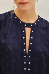 Camisa azul marino de corte holgado con mangas abullonadas, cuello redondo y abertura frontal decorada con tachas metálicas plateadas.