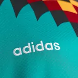 Camiseta de fútbol Adidas retro de la selección de Alemania, diseño alternativo de 1994. Color principal verde turquesa con cuello en V amarillo, rojo y negro, y un llamativo estampado geométrico en el pecho y las mangas en tonos negro, rojo y amarillo.