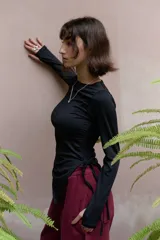 Top de manga larga color negro, confeccionado en jersey elástico. Presenta un diseño asimétrico con jaretas laterales regulables que permiten ajustar el largo y el volumen, y aberturas para los pulgares en los puños.