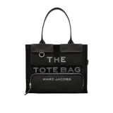 Bolso tipo tote grande de Marc Jacobs, confeccionado en lona de algodón color negro. Presenta diseño utilitario con múltiples bolsillos frontales con solapa, un bolsillo con cierre y el texto "THE TOTE BAG" impreso en contraste. Cuenta con asas superiores dobles.