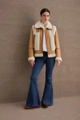 Campera tipo gamulán de cuero color camel con interior y detalles de piel sintética en color crema. Presenta cuello alto con doble hebilla ajustable, cierre frontal con cremallera y bolsillos laterales con cierre.