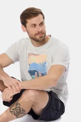 Remera de manga corta color gris con estampado de paisaje costero con palmeras y tablas de surf.