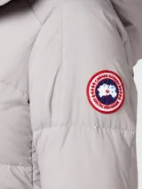 Campera puffer gris claro con capucha, cierre frontal con botones a presión y logo de Canada Goose en el brazo izquierdo.