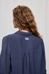 Camisa de manga larga color beige con cuello clásico y botonadura frontal. Presenta mangas con volumen sutil, puños abotonados y una silueta amplia de caída fluida.