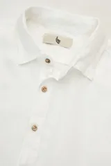 Camisa blanca de manga larga confeccionada en lino 100%, con calce recto y relajado. Presenta frente abotonado con botones de coco con logo y parche Polonio.