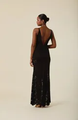 Vestido largo de encaje negro con escote en V y breteles anchos. Presenta un diseño ajustado en el torso que cae con fluidez hacia el ruedo, con una transparencia característica del tejido.