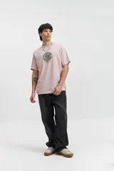 Remera de manga corta color rosa pálido con escote redondo y fit regular. Presenta un arte estampado en relieve en el centro del pecho con texto circular.