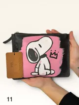 Sobre de cuero marrón con diseño pintado a mano que presenta al personaje Snoopy sobre un fondo rosado y la palabra 'heal'. Cuenta con cierre superior y etiqueta de cuero colgante.