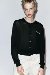 Chaqueta de punto de efecto doble capa color negro, con cuello redondo y ribete blanco, manga larga y cierre frontal con botones. Cuenta con un bolsillo de parche en el pecho con detalle en contraste.