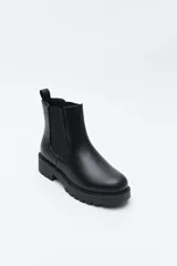 Bota tipo chelsea de caña baja con suela dentada robusta. Presenta un diseño combinado con paneles laterales elásticos, acabado liso en el frente y detalle texturizado en relieve en la parte posterior, incluyendo un tirador trasero para facilitar el calce.