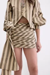 Minifalda de tafeta con diseño de rayas verticales en tonos bronce y beige. Presenta un estilo drapeado con un lazo lateral largo y caída fluida.