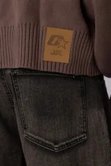 Campera tejida de punto con cierre frontal completo y cuello polo. Presenta un diseño de franja horizontal ancha en color crema con estampado gráfico oscuro sobre una base de color marrón. Posee puños y ruedo acanalados, con un pequeño parche de marca en el puño izquierdo.