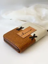 Billetera pequeña de cuero color camel y crudo, con cierre metálico y detalle de cruces bordadas en hilo negro.