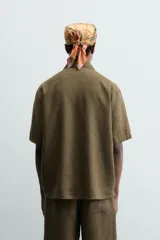 Camisa de corte relajado confeccionada en lino color verde militar, con cuello solapa, manga corta y cierre frontal de botones.