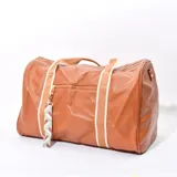 Bolso tipo duffel color marrón con textura símil cuero, doble asa de mano con refuerzo y correa de hombro desmontable. Tiene un bolsillo externo con cierre y llavero decorativo.