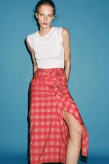 Falda midi de tiro medio, con estampado a cuadros vichy en tonos rojo y rosado, detalle de volantes en el delantero y cierre lateral con cremallera oculta.