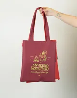 Tote bag de tela color rojo con estampado gráfico en color verde lima que representa una fogata y una persona sentada tomando una bebida caliente, acompañado por el texto 'Invierno Uruguayo'.