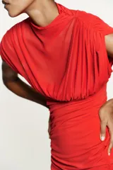 Vestido corto rojo confeccionado en tejido mesh. Cuello alto y manga sisa con frunces. Bajo combinado a tono con drapeado a los lados. Cierre lateral con cremallera oculta en costura.