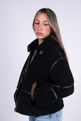 Campera de corderito negra con detalles de ribetes en símil cuero marrón, cuello alto con hebilla y cierre frontal metálico.