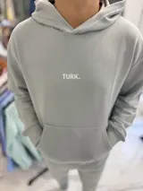 Conjunto de jogging celeste claro compuesto por un canguro con capucha y bolsillo tipo canguro con estampa pequeña del texto "TURK.", y un pantalón de jogging con puños elásticos en los tobillos.