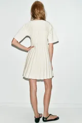 Vestido corto de punto rib color crema, con cuello redondo, manga corta abullonada y falda plisada.