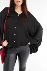 Camisa negra de satén con cuello clásico, corte holgado y cierre frontal con botones blancos.