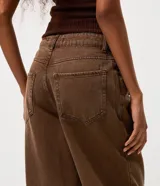 Pantalón de jean color marrón con corte baggy holgado, tiro medio y cierre frontal con cremallera y botón. Incluye un pañuelo estampado decorativo en la cintura.