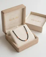 Collar de diseño minimalista compuesto por pequeñas cuentas negras intercaladas con cuentas cilíndricas de piedra natural en tono coral y detalles en dorado.
