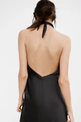 Vestido largo de satén con cuello halter y escote fluido. Presenta un diseño de espalda descubierta con cierre de cremallera oculta y lazada ajustable en el cuello.
