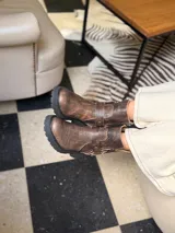 Bota corta de cuero vacuno en color chocolate con efecto desgastado. Presenta una suela track de goma negra, detalle de pulsera desmontable con tachas metálicas y cierre lateral.